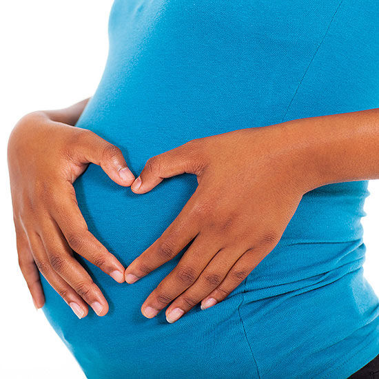 Pregnant woman in blue shirt with hands making a heart shape over belly.